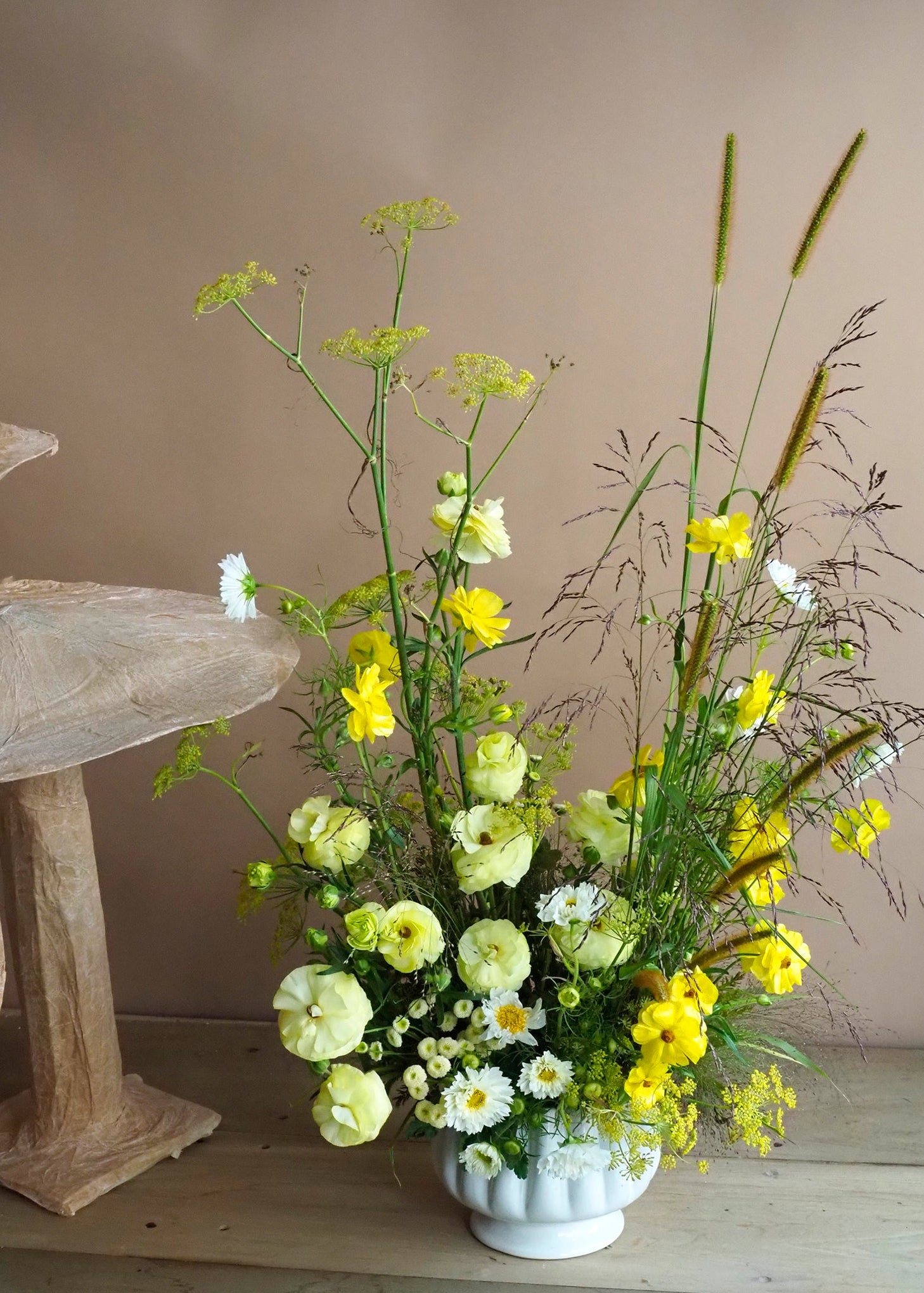 Floral arrangement in a white vase on a wooden surface with a neutral background