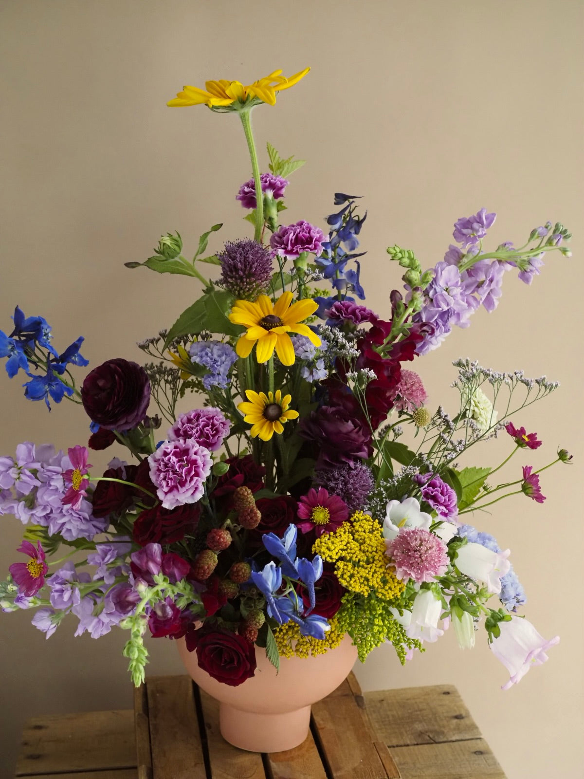 Colorful flower arrangement in a terracotta pot on a wooden surface with a beige background